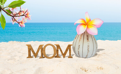 Mom wooden text with plumeria flower in design vase on tropical beach, outdoor day light, Happy Mother's day card background idea