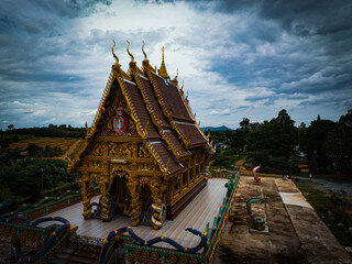 Chachoengsao, Thailand, 28 July 2023. Wat Khao Tham Raet, Golden temple on a hilltop. The temple has a tiered roof with serpent-like figures adorning the ridges. 