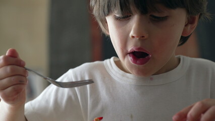 Little boy eating pieces of strawberry with fork, child enjoys sweet dessert after mealtime, kid...
