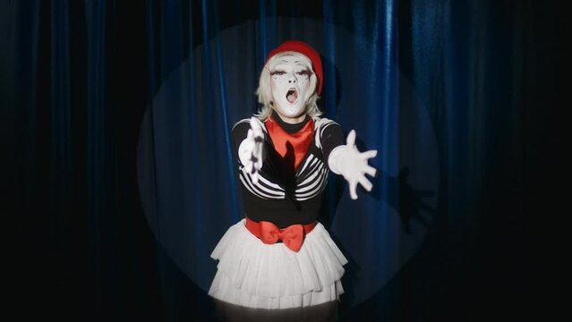 Expressive female mime artist standing in spotlight, showing air kisses and hugs on camera while improvising on theatre stage