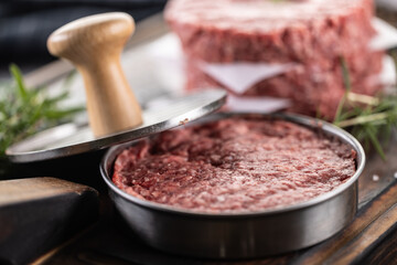 Fresh raw ground beef patties with rosemary salt and pepper made in a meat form on a cutting board - 786375810
