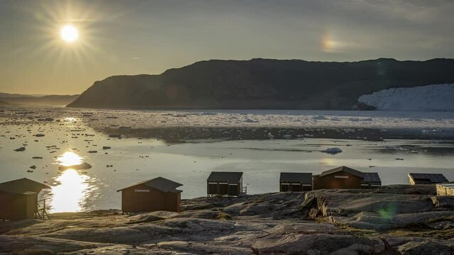 Zeitraffer von Sonnenuntergang und Sonnenaufgang der Mitternachtssonne beim Eqi Gletscher in Gr&ouml;nland, Mitternachtssonne und Halo spiegeln sich im Meer, viele Blendensterne der Mitternachtssonne