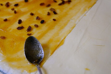 Raw sweet yeast dough on a baking sheet with spoon, filling with raisin and orange jam. Preparation...
