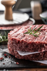 Fresh raw ground beef patties with rosemary salt and pepper made in a meat form on a cutting board - 786376404