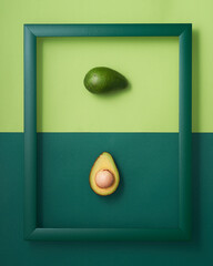 Avocado in wooden picture frame on two-tone green background