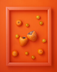 Persimmons, clementines, cherry tomatoes in frame on orange