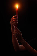 Woman’s hands holding red wax candle burning brightly on black