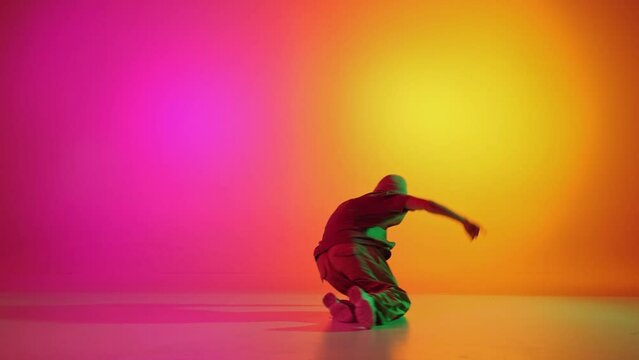 Talented, modern dancer break-dancer spinning on head in motion in neon light against gradient pink-yellow background. Concept of hobby, sport, creativity, fashion and style, motion, action. Ad