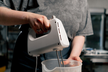close up female baker in a professional kitchen whips paste for cream on a cake with a mixer