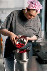 female baker in a professional kitchen pours frozen cherries into a bowl on a scale