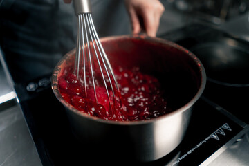 close-up in a professional kitchen hands pour milk into a pan with cherries stirring