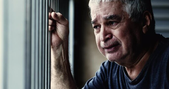 Desperate senior man crying in sorrow and depression depicting illness in old age. 70s tearful older man close-up face gripping on metal bar feeling trapped and shame about past regrets