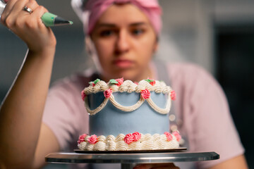 close up of a female baker in a professional kitchen decorating a blue cake with cream
