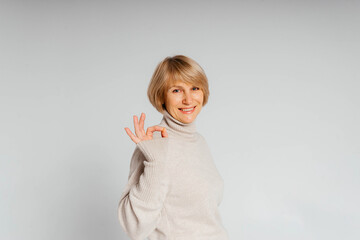 Beautiful adult woman good looking standing on white font smiling and showing excellence sigh in white sweater and white background 