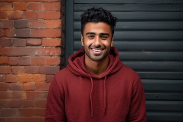 Portrait of a happy indian man in his 20s sporting a comfortable hoodie on vintage brick wall