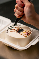 close-up of a female baker in a professional kitchen drawing a dog on a cake with cream