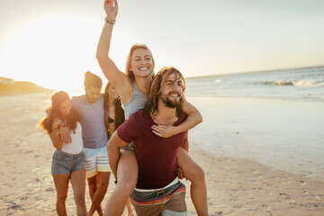 Group of friends running and laughing on the beach at sunset