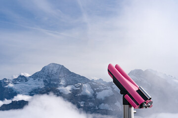 Pink tower viewer binoculars on top of a mountain  in Switzerland. View of Swiss Alps. Copy space on the left