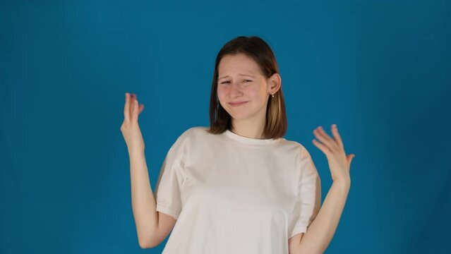 Joyful young woman gestures standing on blue background. Positive lady in white t-shirt expresses joy in studio. Happiness and good mood