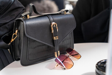 Black women's handbag and a pair of retro sunglasses on a cafe table