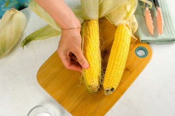 Woman hands peeling fresh ear of corn removing leaves on cutting board cooking on kitchen. Cuisine culinary prepare cook dish domestic food recipe ingredients. Healthy nutrition eating with vegetables