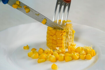 Woman cutting piece of baked corn on plate on kitchen at home, hand close-up. Prepare cook bake dish. Cuisine culinary nutrition domestic food recipe ingredients vegetable. Cooked sweet corn.