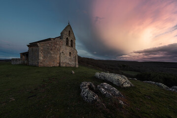 Fototapeta premium Sunset with dramatic sky in the Romanesque church of San Martín, in Quintanilla de la Berzosa, Aguilar de Campoo, Palencia, Castilla y León, with the tombs of the medieval necropolis in the foreground