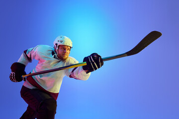 Ambitious man, hockey player posing with stick, showing his determination against gradient blue...