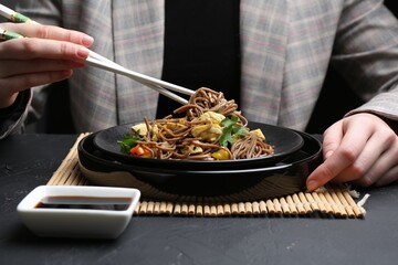 Stir-fry. Woman eating tasty noodles with meat and vegetables at dark textured table, closeup