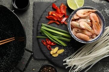 Flat lay composition with black wok, spices and products on dark textured table