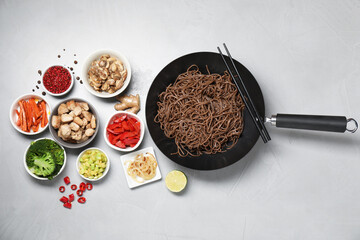 Wok with noodles, chicken and other products on light grey table, flat lay