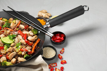 Stir-fry. Tasty noodles with meat in wok, chopsticks and ingredients on grey textured table