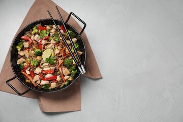 Stir-fry. Tasty noodles with meat in wok and chopsticks on grey textured table, top view. Space for text