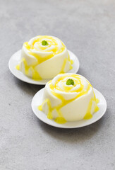 Modern dessert. Lemon cream pudding, Panna Cotta in the shape of a rose, with lemon sauce. Light grey background. Close-up