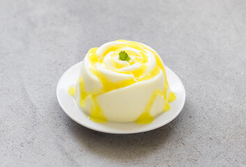 Lemon cream Panna Cotta in the shape of a rose, with lemon sauce. Light grey background. Close-up