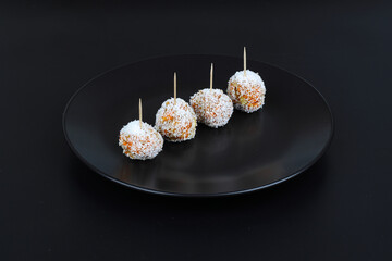 Beautiful sweets with coconut on a black plate on a black background close-up