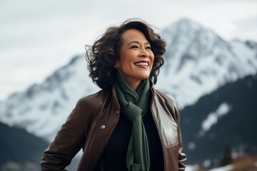 Obraz premium Portrait of a smiling woman in her 50s sporting a stylish leather blazer over snowy mountain range