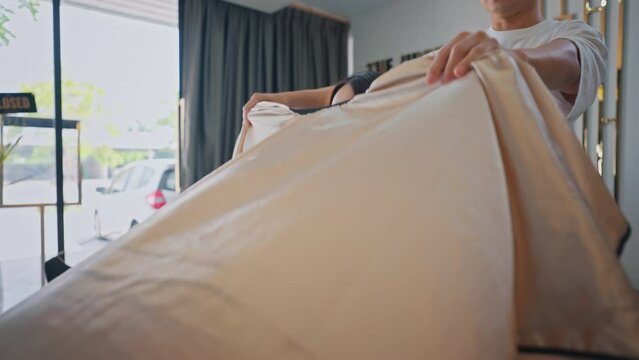 Asian Hairdresser man puts on protective cape apron to woman customer at beauty salon or barber shop.