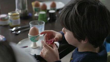 Back of little boy eating toast with jelly seated at breakfast table, close-up of 5 year old boy...