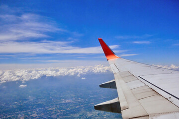 a view from airplane window that has a wing with red winglet in the sky with cloud and city below