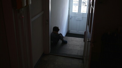 Child seated alone in dark corridor struggles with emotional despair covering face wth hands....
