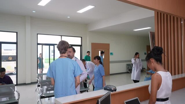 Group of physicians and patients people in waiting area in busy hospital, many patients waiting in queue to visit doctors at reception desk, medical trainee man consult senior surgeon in sickness case