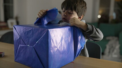 Child unwrapping present gift, one small boy tearing paper from package eagerly wanting to open box