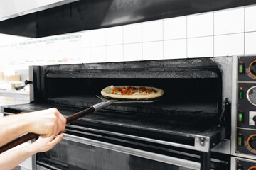 Pizzamaker worker puts pizza into an electric oven, business pizzeria concept