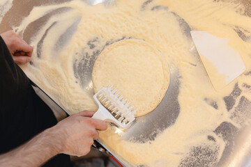 Pizzamaker stretches dough, worker removes air with roller from fresh food pizza, top view. Business pizzeria concept