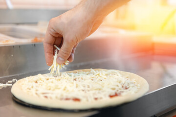 Pizzamaker worker preparing fresh food pizza adds toppings with mozzarella cheese, top view. Business pizzeria concept.