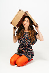 Woman Balancing Vintage Suitcase on Head While Sitting Against White Background
