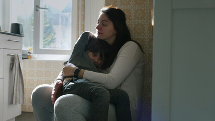 Mother holding child in arms leaning on kitchen wall resting together with eyes closed. Candid...