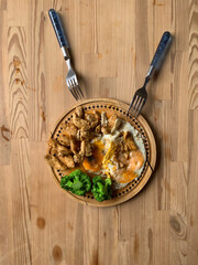 Old cracked wooden round board with lunch on an old kitchen wooden table. Scrambled eggs, broccoli and fried chicken breast pieces and two forks. Still life dinner for two