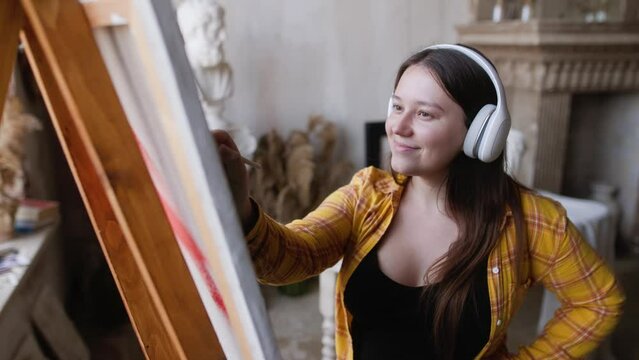 Girl paints a picture in a creative setting in an artist's studio. Funny dance.